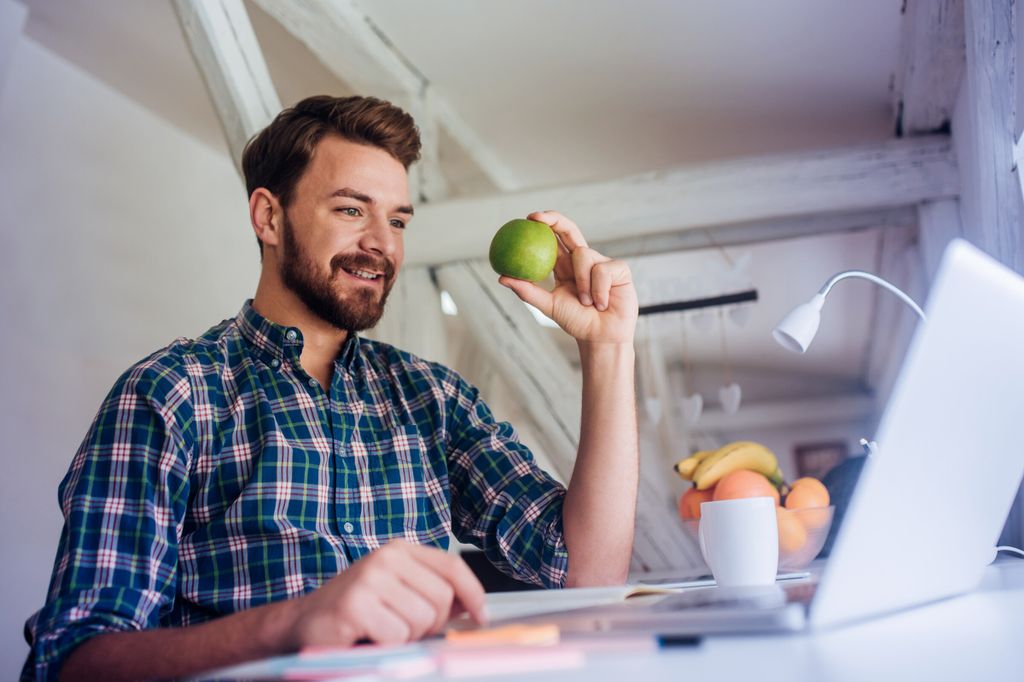 Mann am Laptop mit Apfel in Hand
